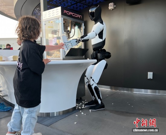 图为特斯拉首家超级充电站餐厅内，特斯拉人形机器人“Optimus”给小朋友派发爆米花。中新社记者 张朔 摄